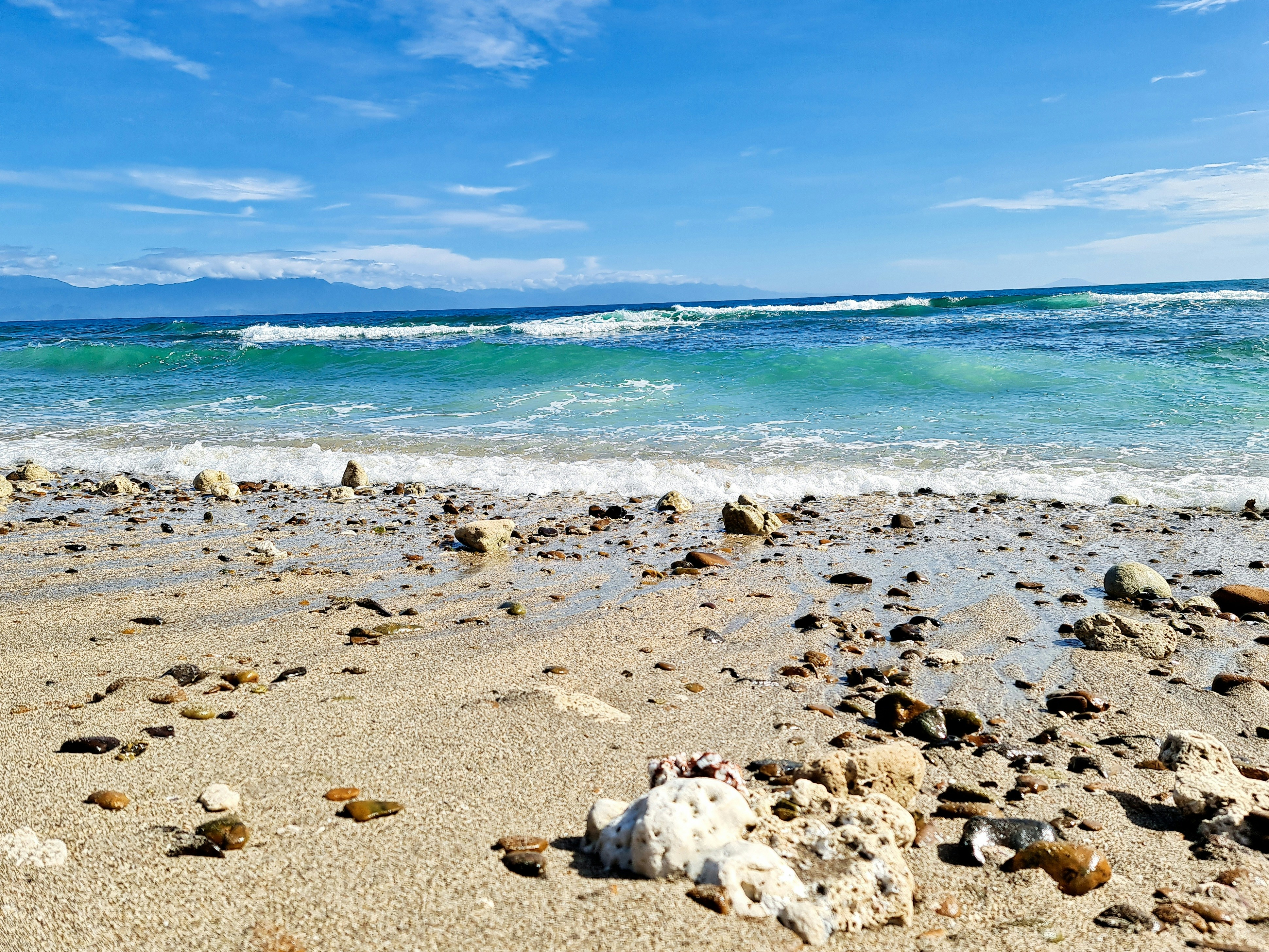 a sandy beach with rocks and water in the background