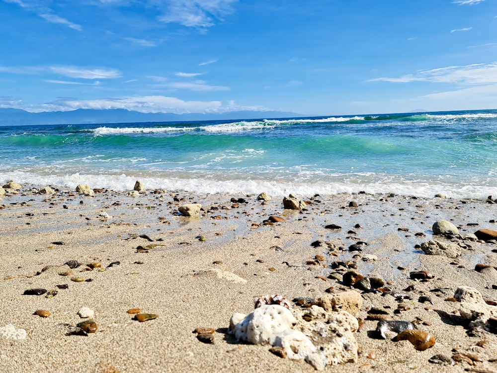 a sandy beach with rocks and water in the background