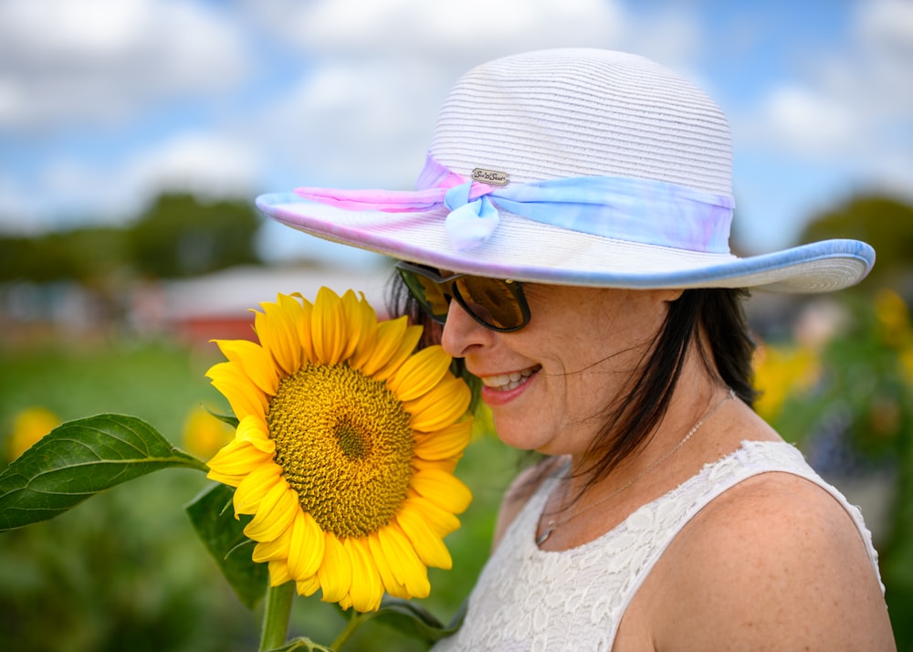 a woman wearing a hat and sunglasses holding a sunflower