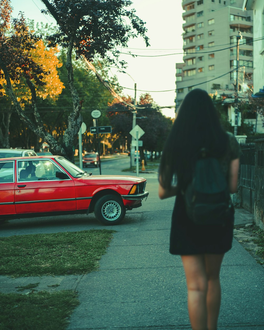 a woman walking down a sidewalk next to a red car