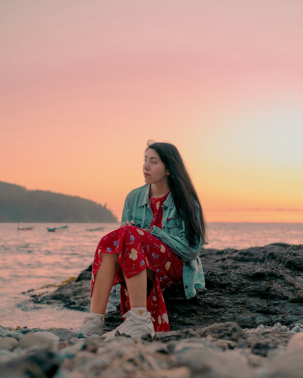 a woman sitting on a rock near the ocean