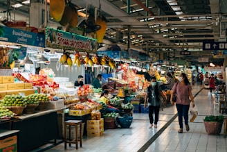 two people walking through a market with fruit and vegetables
