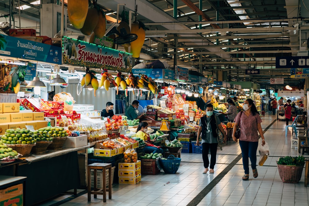 two people walking through a market with fruit and vegetables