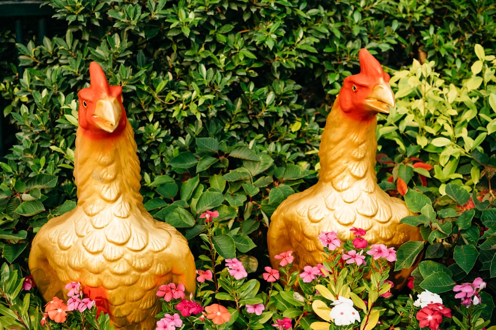 two golden rooster statues in a garden of flowers