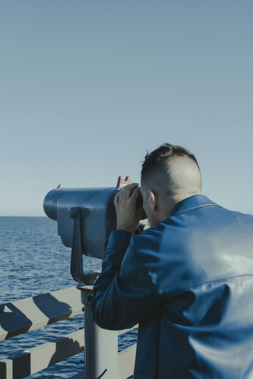 a man looking through a telescope at the ocean
