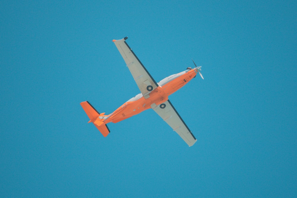 an orange and white airplane flying in a blue sky