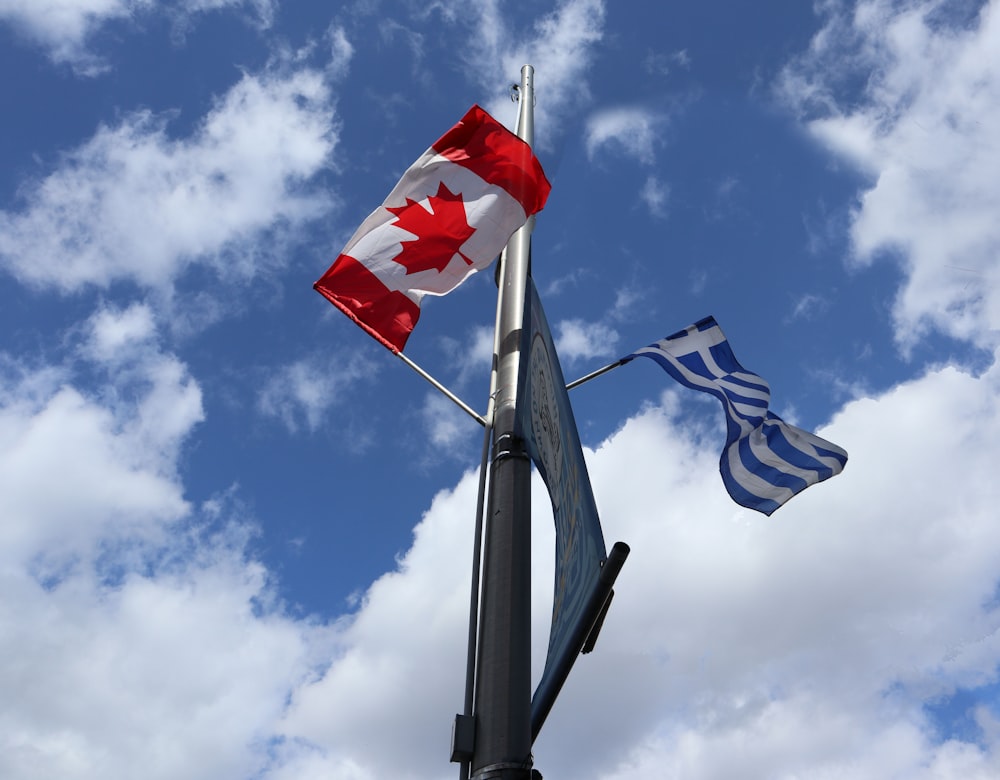 two canadian and greek flags flying in the wind