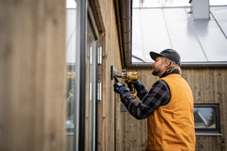 A professional construction worker operating a core drilling machine on a concrete wall.