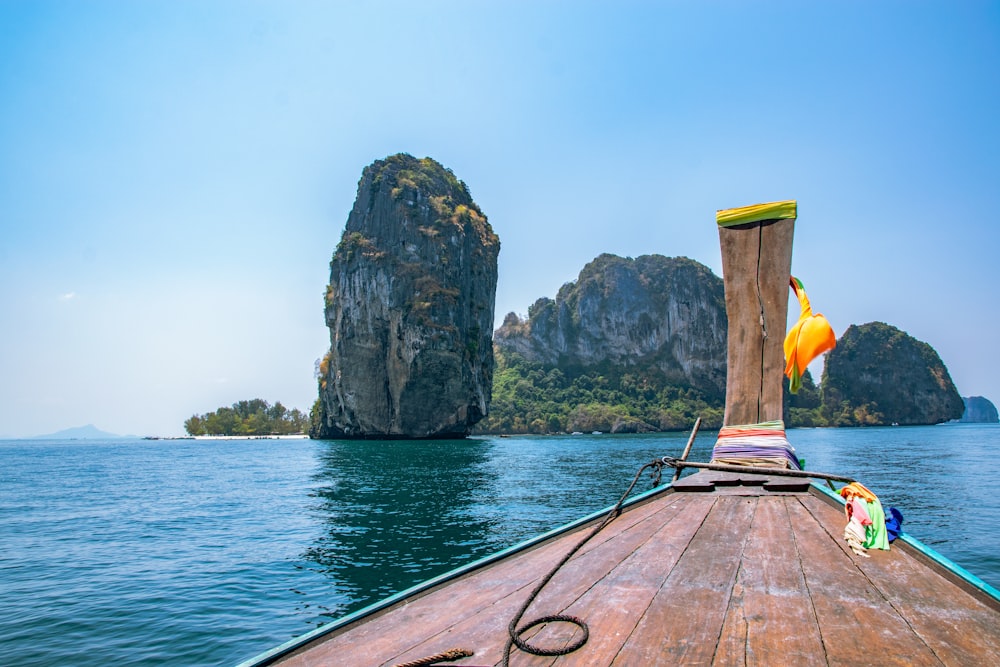 a wooden boat traveling past a large rock formation in the ocean