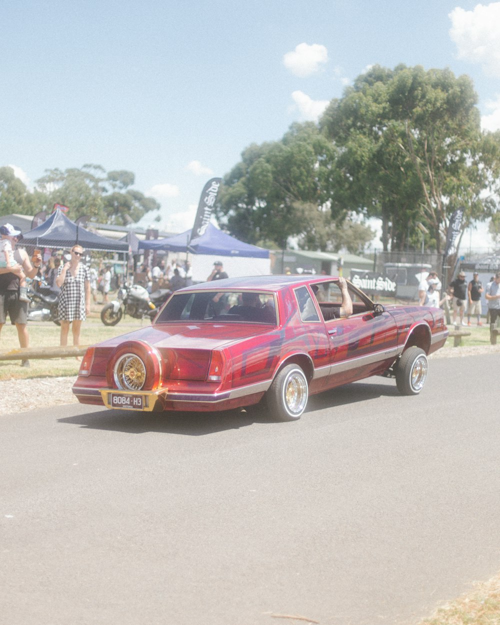 a red car driving down a street next to a crowd of people