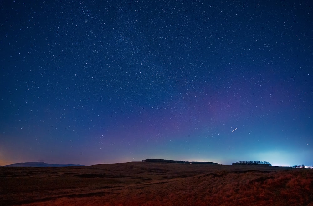 the night sky with stars above a field