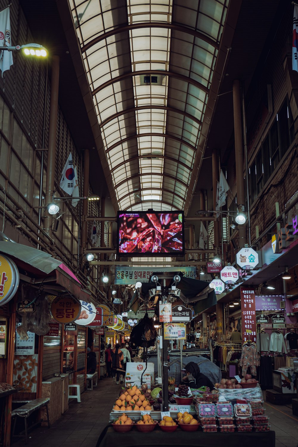 an indoor market with a large screen on the ceiling