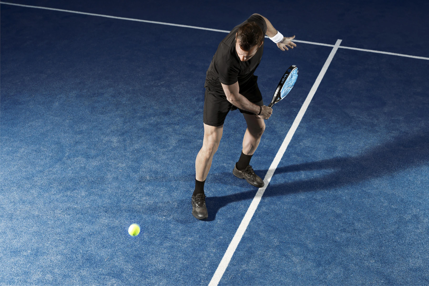 A man seen from above bending to a ball beside a white line on blue turf
