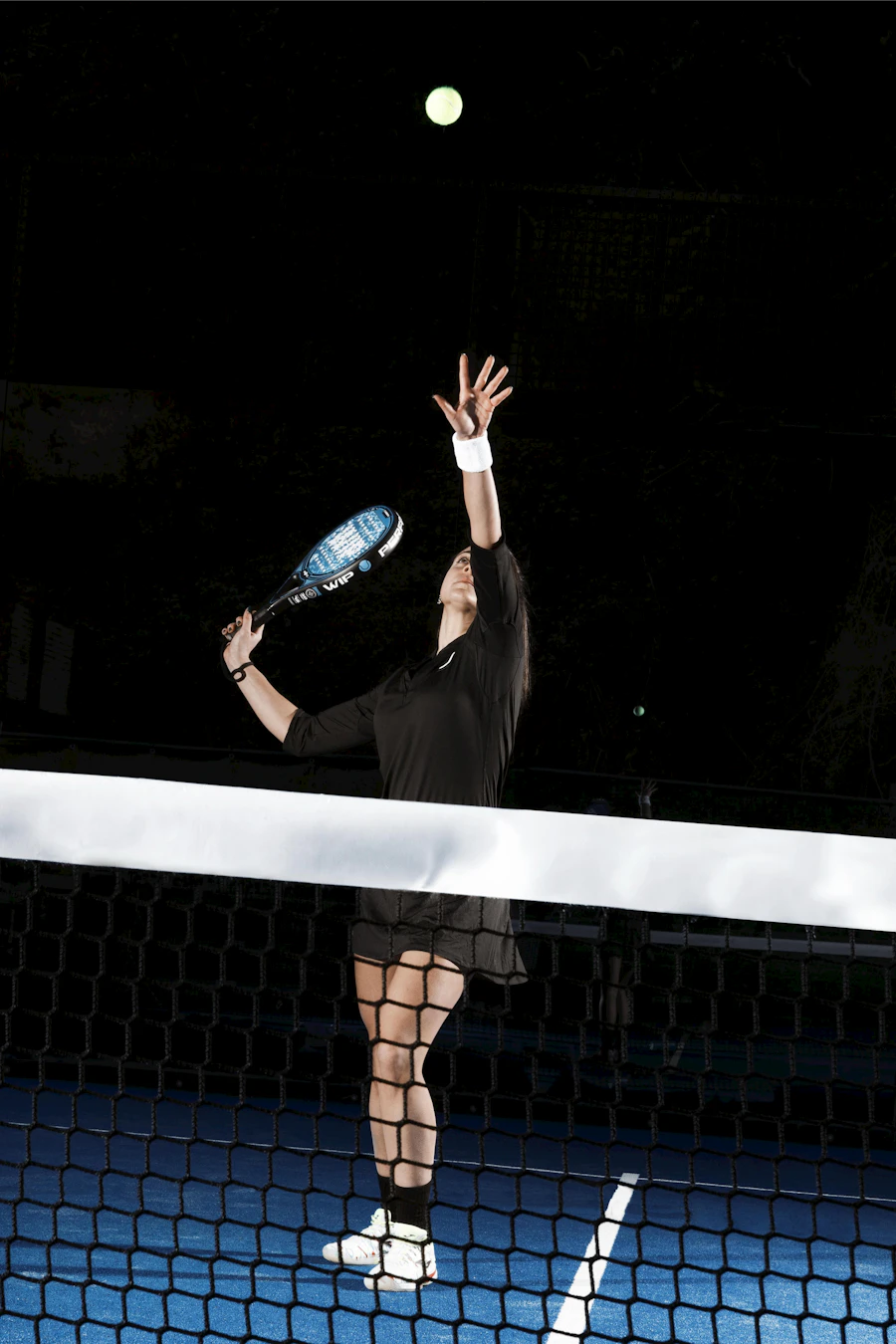 Padel player serving at night under court lights