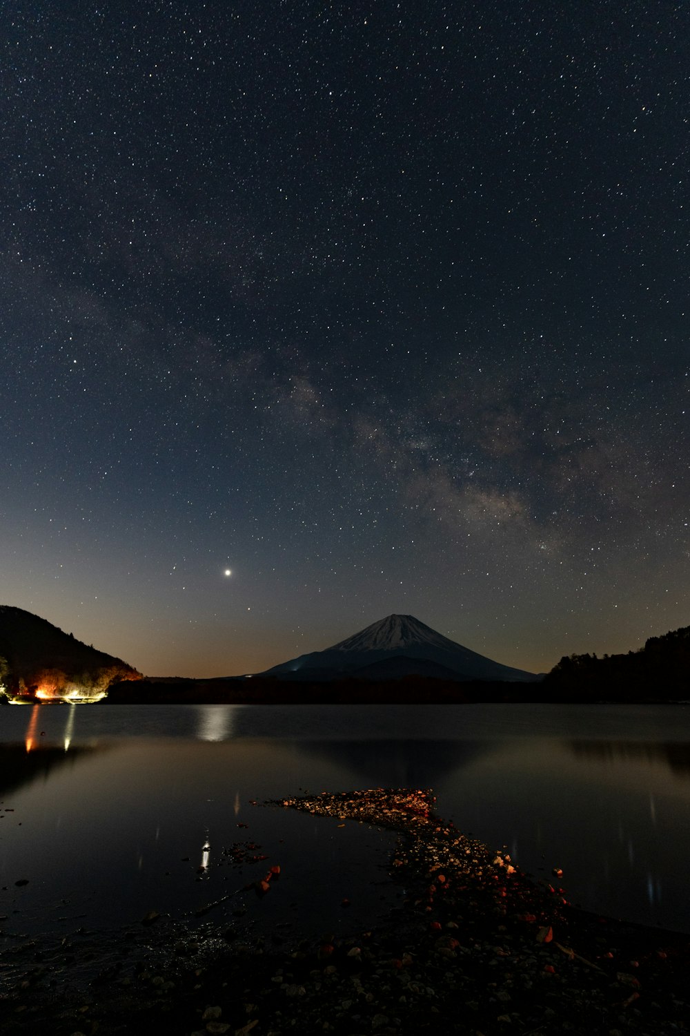 the night sky over a lake with a mountain in the background