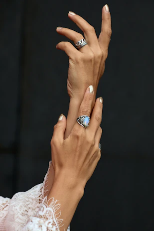 Elegant hands adorned with Varica Jewels rings, holding a white silk fabric softly lit in warm tones.