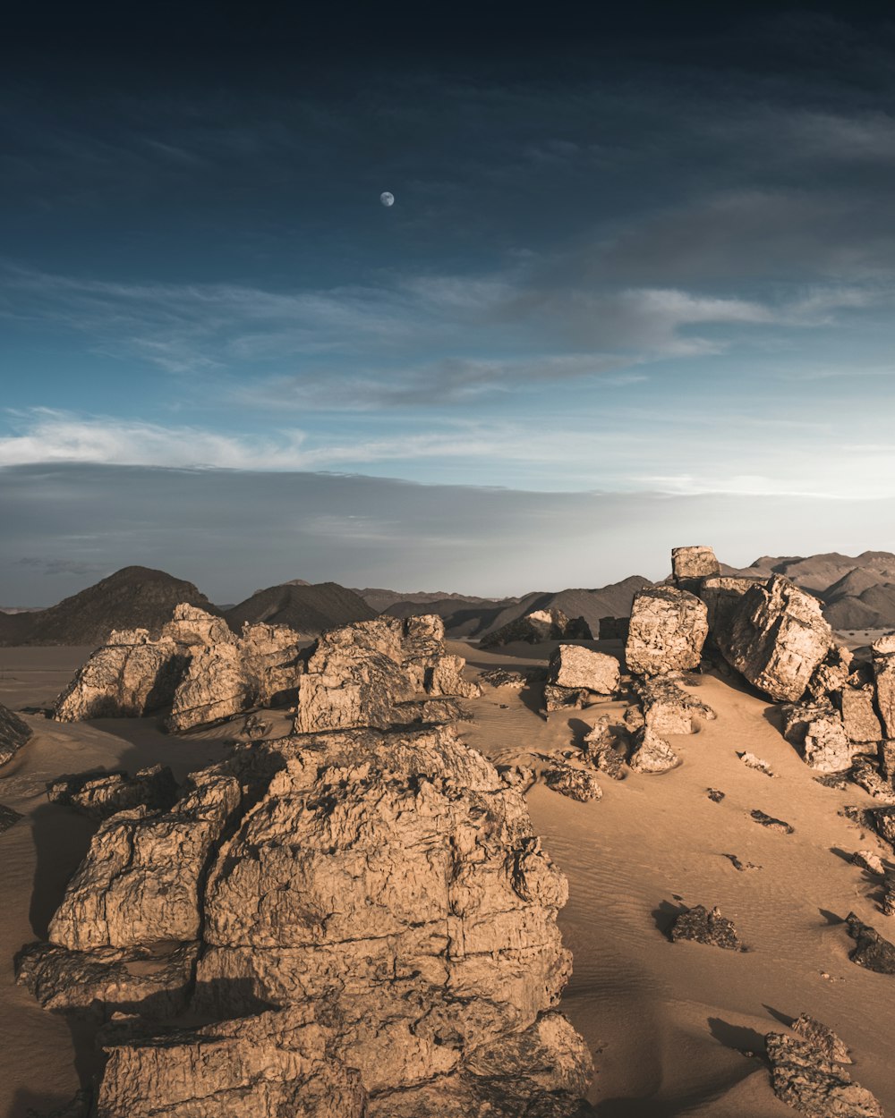a desert landscape with rocks and a moon in the sky