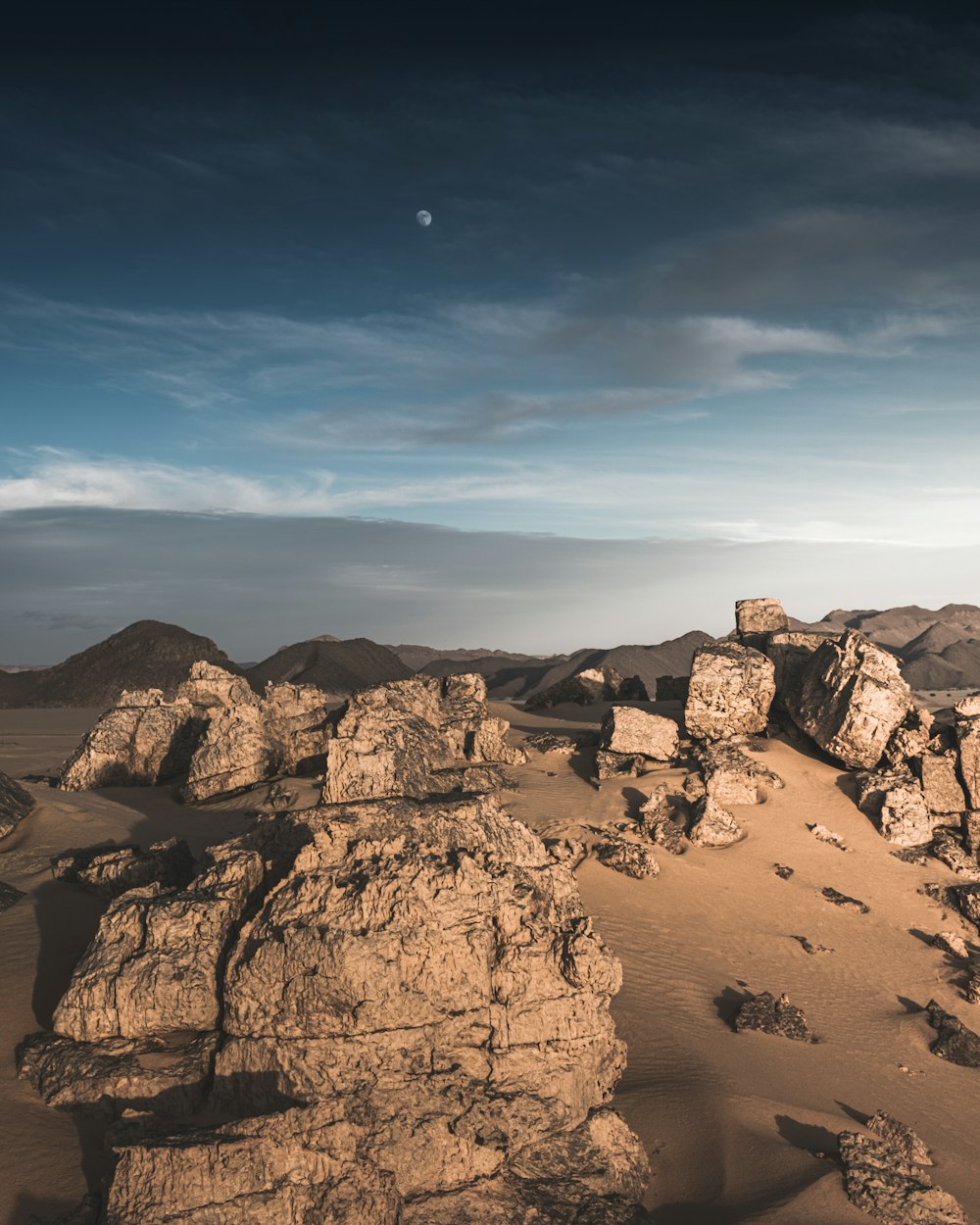 Un paisaje desértico con rocas y una luna en el cielo