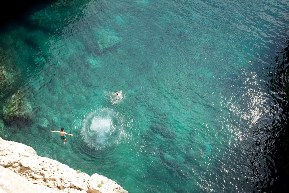 two people swimming in the water near a cliff