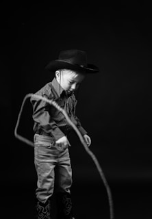 a young boy wearing a cowboy hat and holding a rope