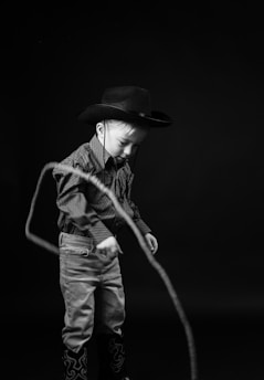 a young boy wearing a cowboy hat and holding a rope