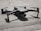 A small gray quadcopter drone with labeled 'Mavic 2' rests on a rough concrete surface. The drone has four rotors, with two angled slightly upward. Its compact form and camera at the front are highlighted by the shadows cast beneath it.