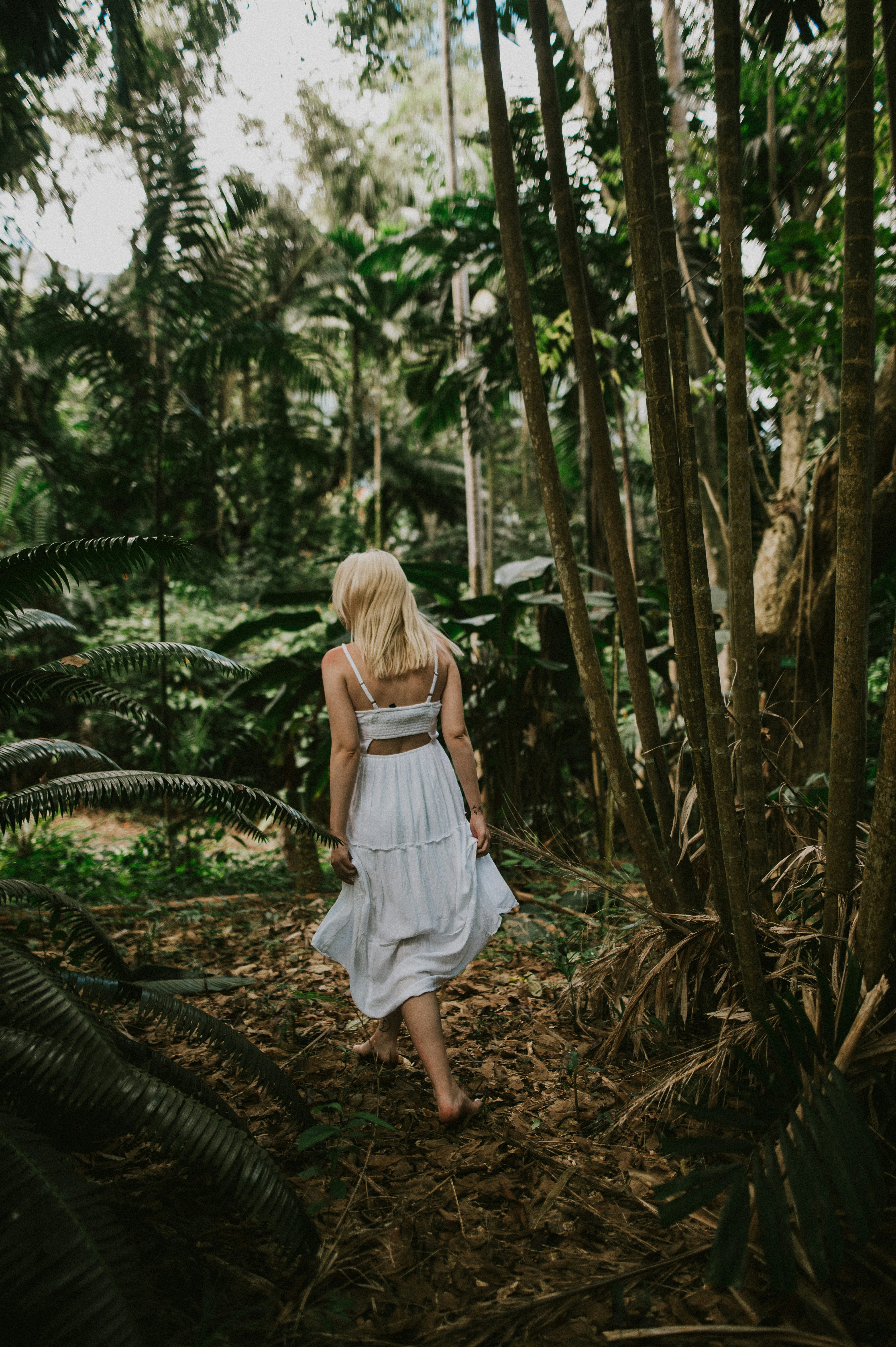 a woman in a white dress walking through a forest