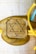 A gold-colored decorative piece features a prominent Star of David symbol in the center. It is attached to strings of different colors: yellow and blue, suggesting a handmade or artistic element.