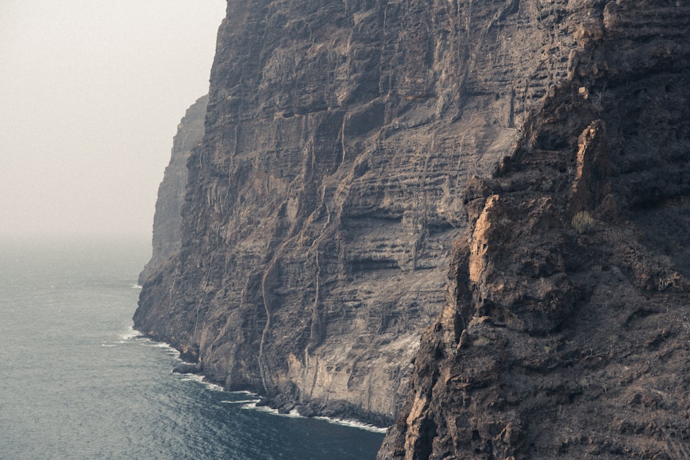 a large cliff next to the ocean on a foggy day