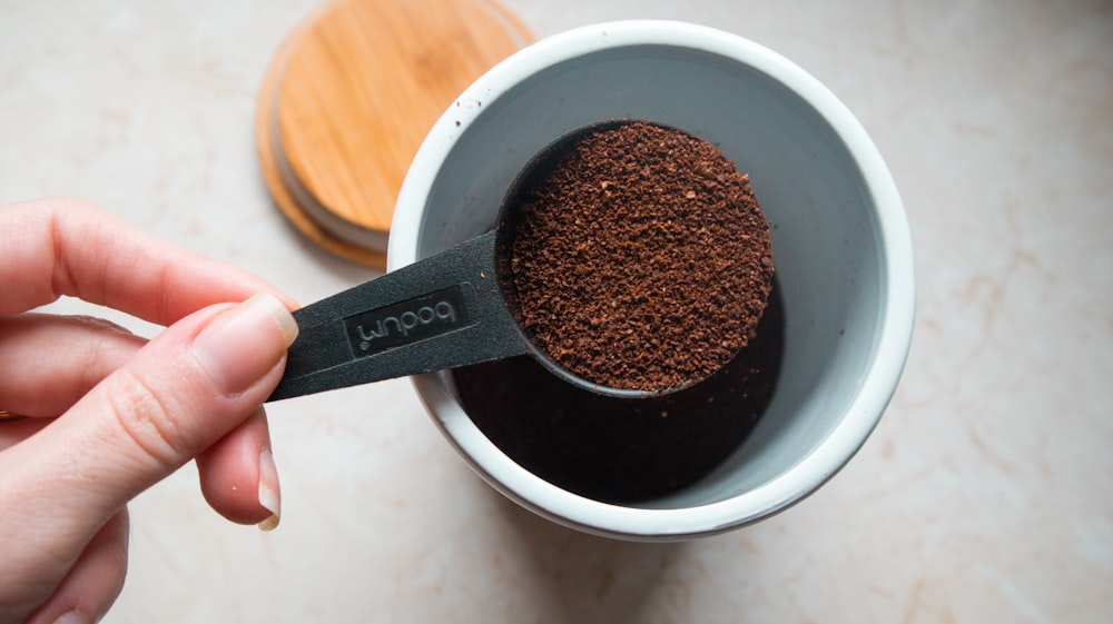 a person holding a measuring spoon over a cup of coffee