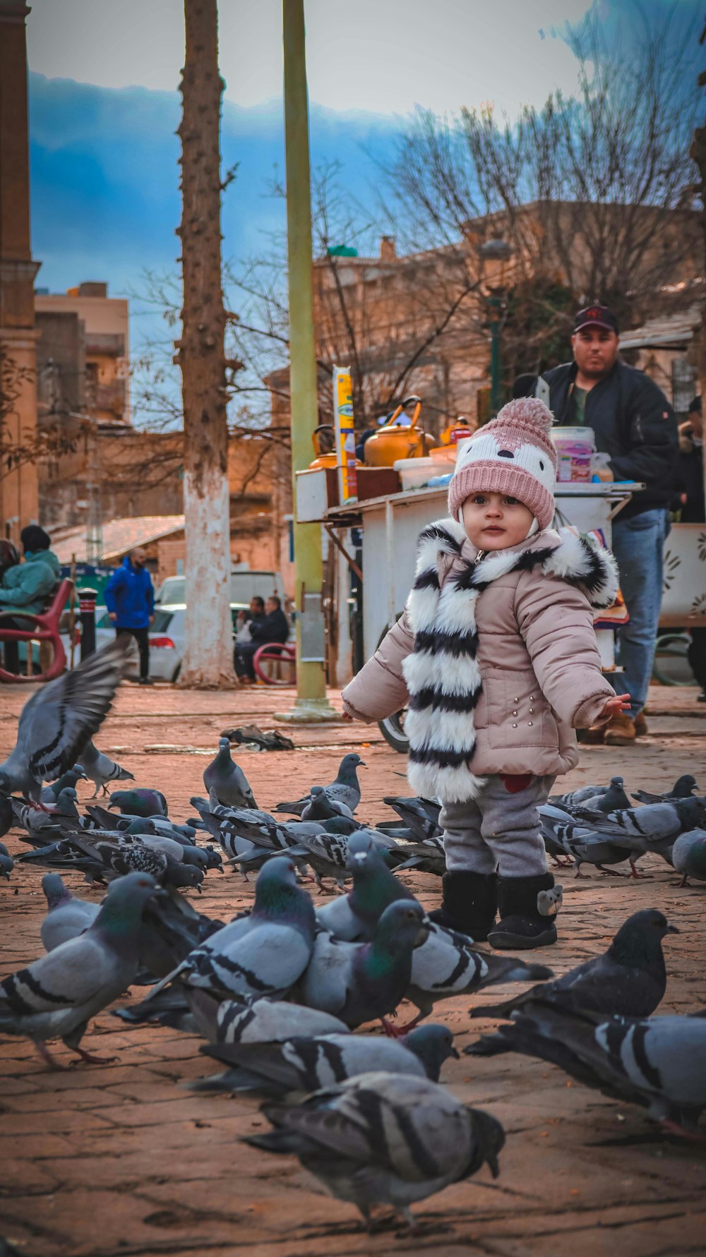 a little girl standing in front of a flock of pigeons