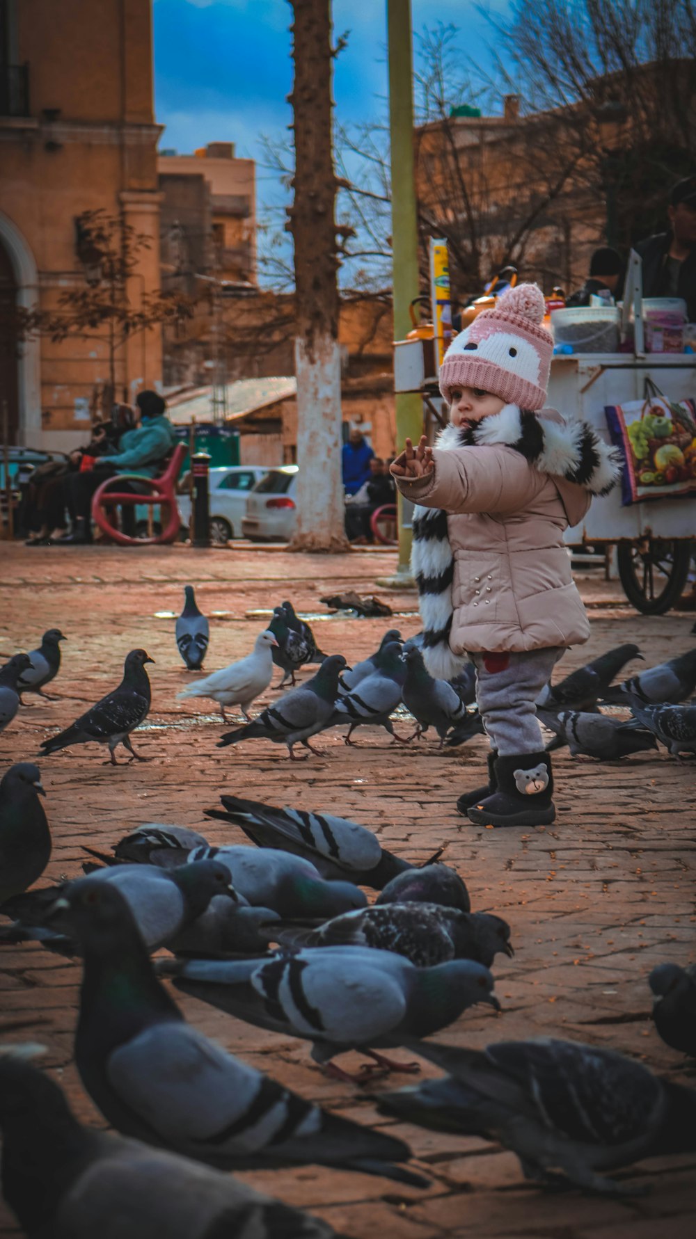 a little girl standing in front of a flock of pigeons