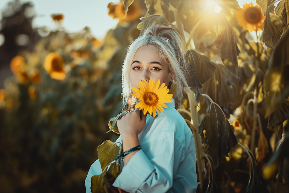 a woman holding a sunflower in front of a field of sunflowers