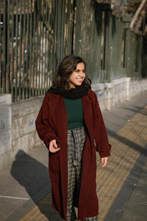 A candid shot of a woman walking through a sunlit park wearing a flowing trench coat in muted colors.