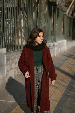 A candid shot of a woman walking through a sunlit park wearing a flowing trench coat in muted colors.