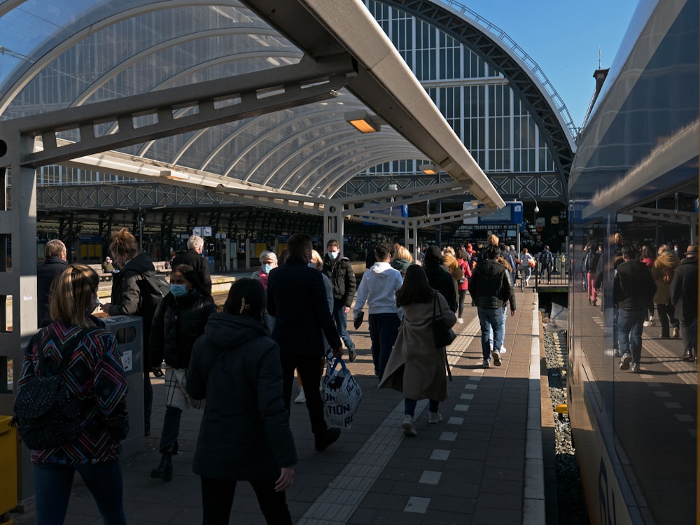 a group of people walking down a sidewalk next to a train station