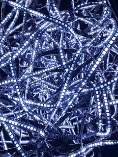 A complex tangle of illuminated LED light strips in various directions, creating a dense and intricate pattern against a dark background.