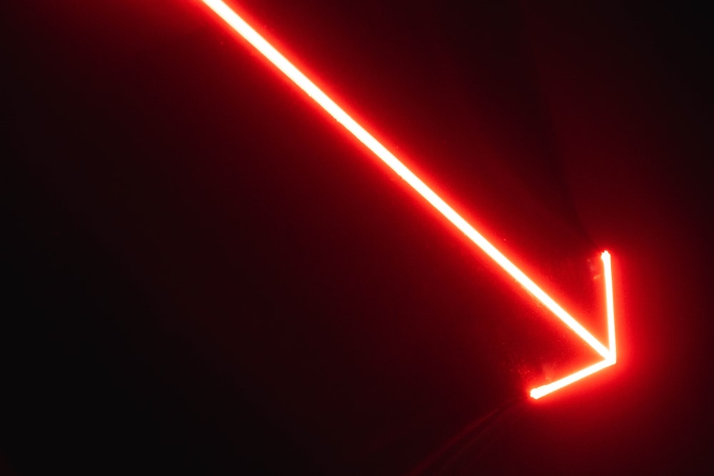 a red neon arrow pointing upward in the dark