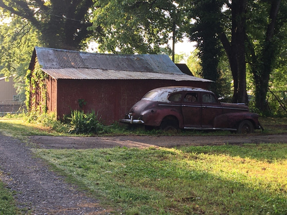 an old car parked in front of a barn