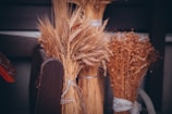 Bundles of wheat and dried plants are neatly tied together, set against a wooden or dark background. The scene suggests a rustic or agricultural setting, exuding a sense of harvest and countryside charm.