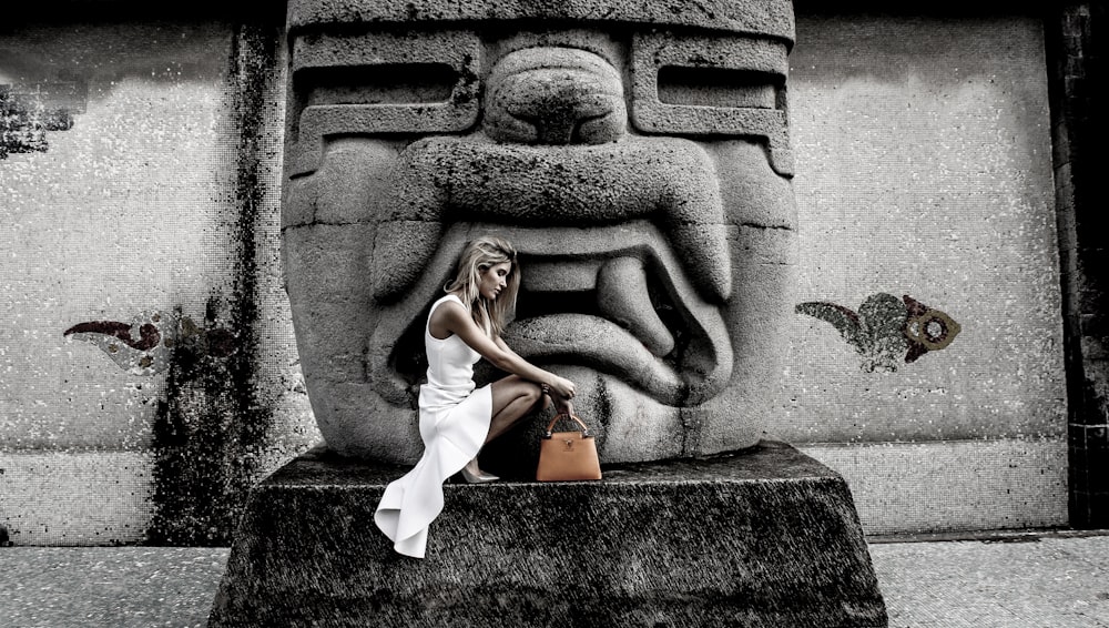 Une femme en robe blanche assise sur une statue de pierre