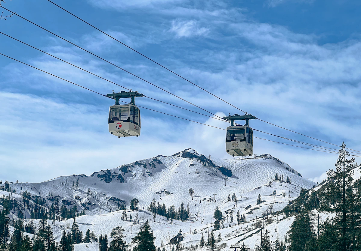 Two gondola cabins crossing above snow-covered mountain peaks under a blue sky