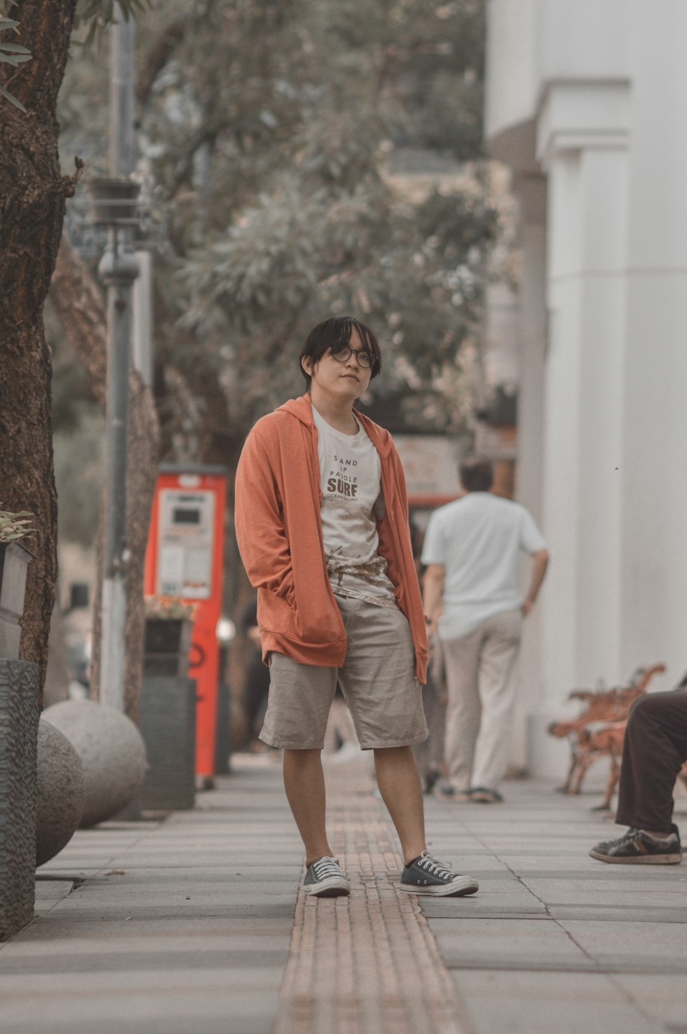 a man standing on a sidewalk next to a tree