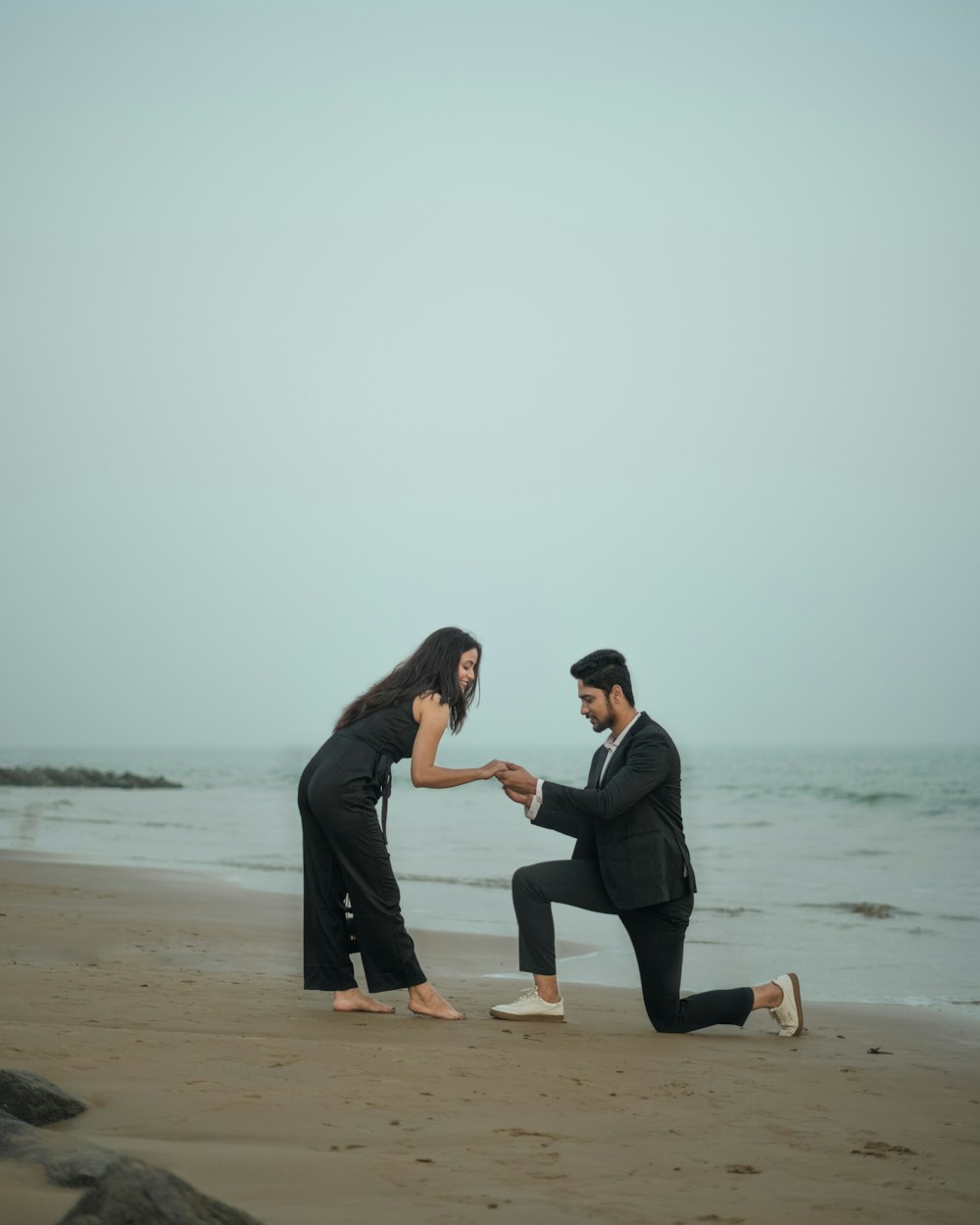 a man kneeling down next to a woman on a beach