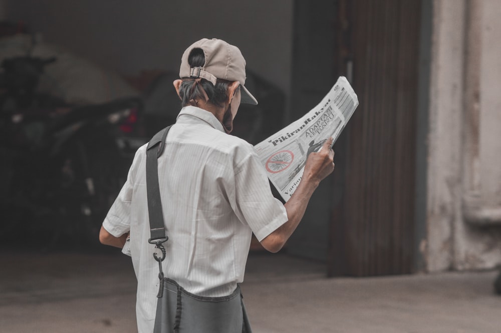 a man reading a newspaper while wearing a hat