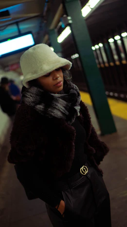 A model wearing a vintage-inspired dad hat in muted earth tones, standing on a graffiti-covered subway platform.