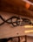A wooden surface with a cluster of black cables fastened by cable ties. The cables are secured against the brown wooden texture with screws partially visible. Warm light reflects off the surface, casting a soft glow. The background shows part of a floor and furniture legs.