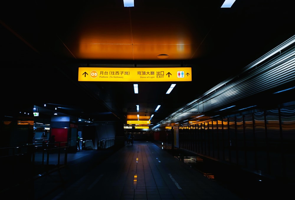 a dimly lit subway station with a yellow sign above it