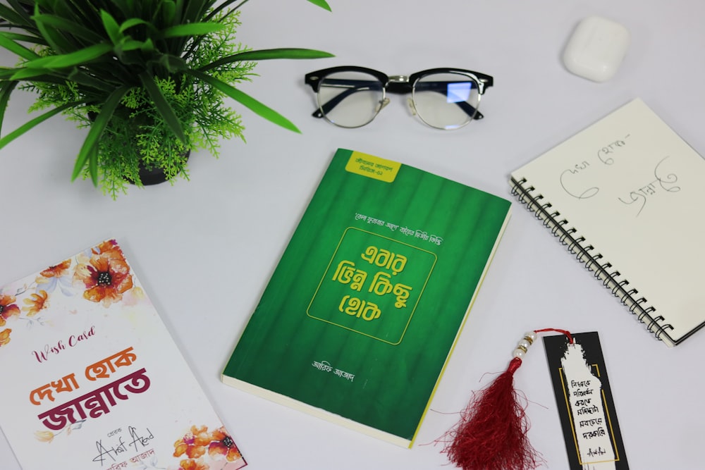 a table with a book, pen, eyeglasses and a plant