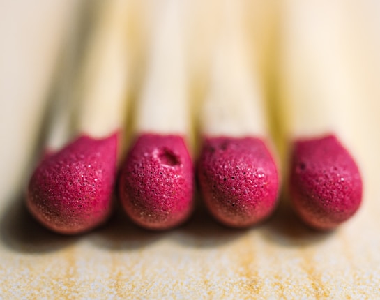 A close-up view of four match heads lined up in a row, focusing on their textured red tips. The background is softly blurred, highlighting the sharp detail on the match heads.